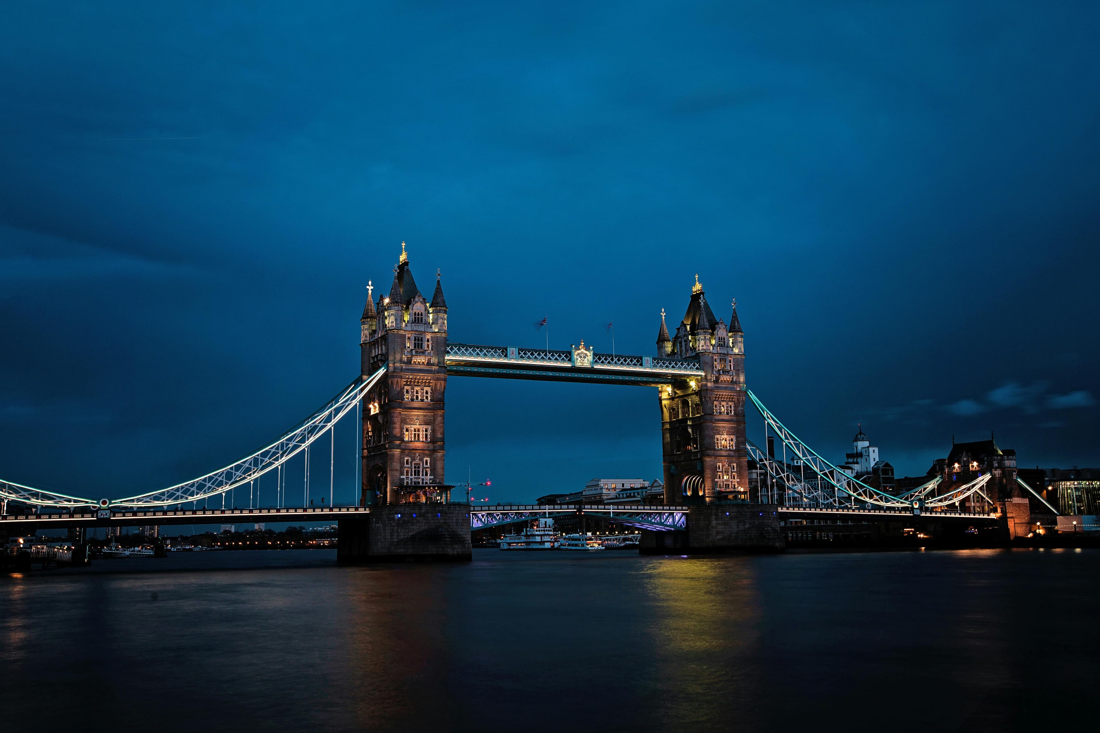 Tower Bridge in London illuminated at night with lights reflecting on the calm River Thames.