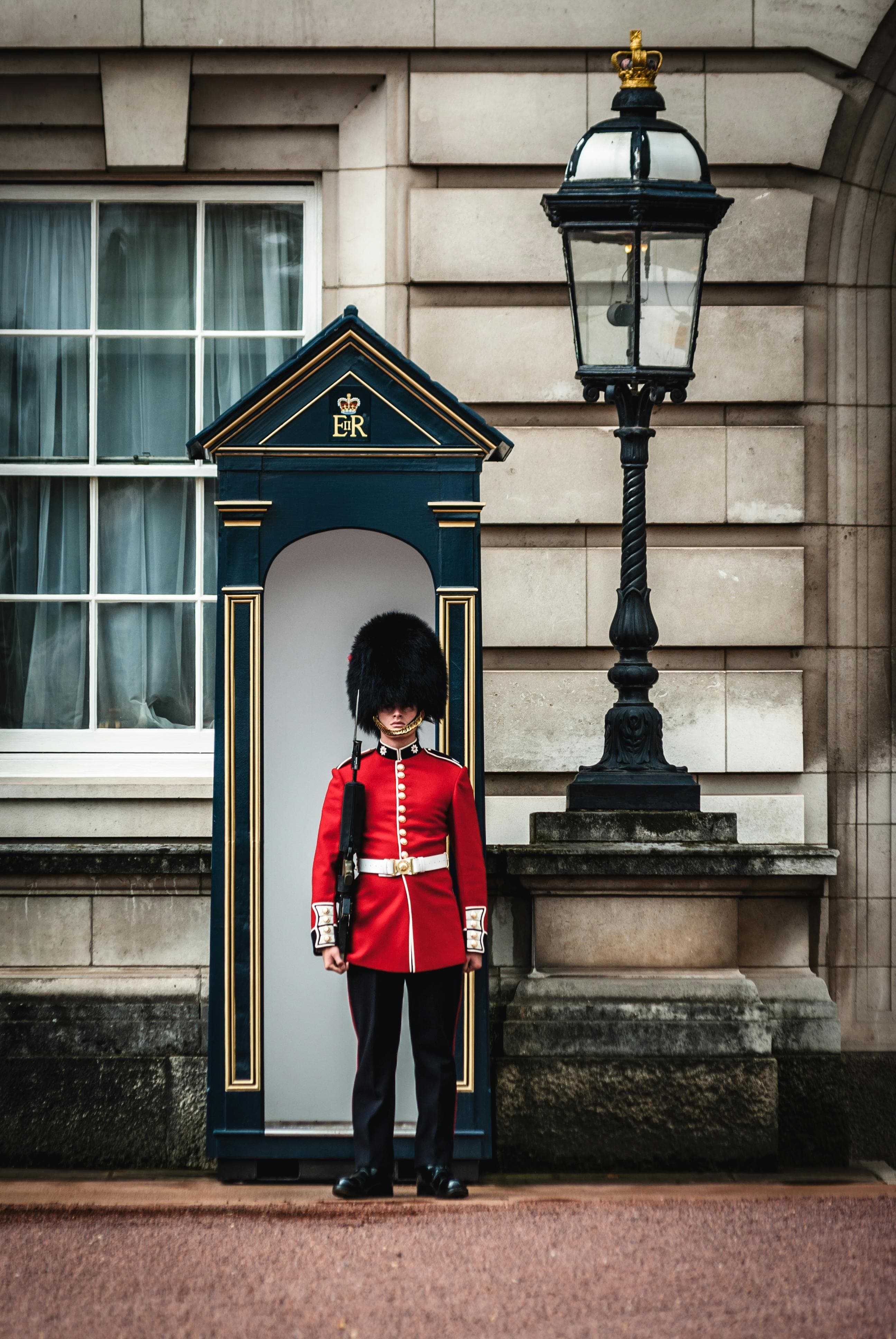 Royal Guard in red tunic and bearskin hat stands at attention beside a sentry box.