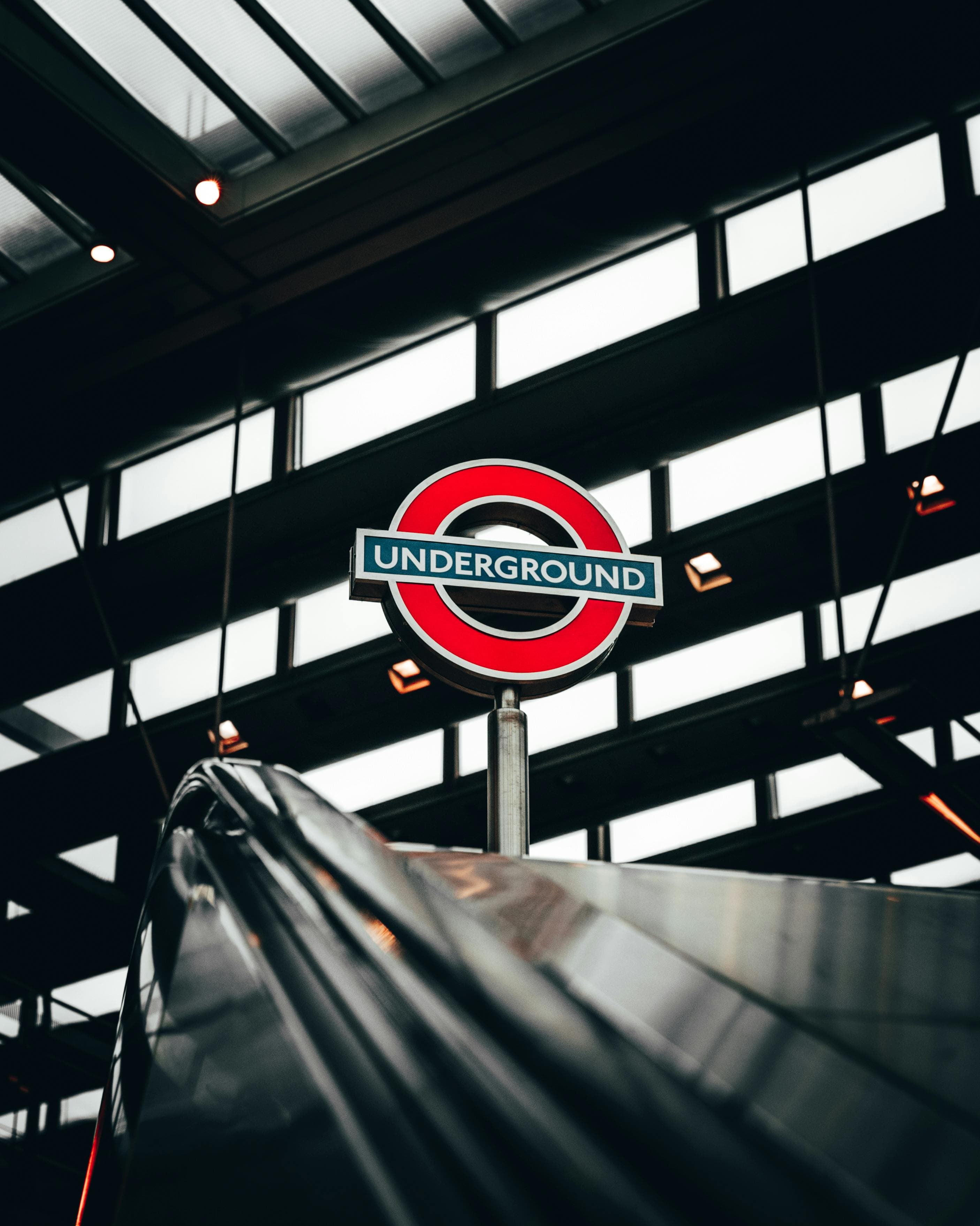 Iconic London Underground roundel sign stands above a metallic escalator in a modern transit station.